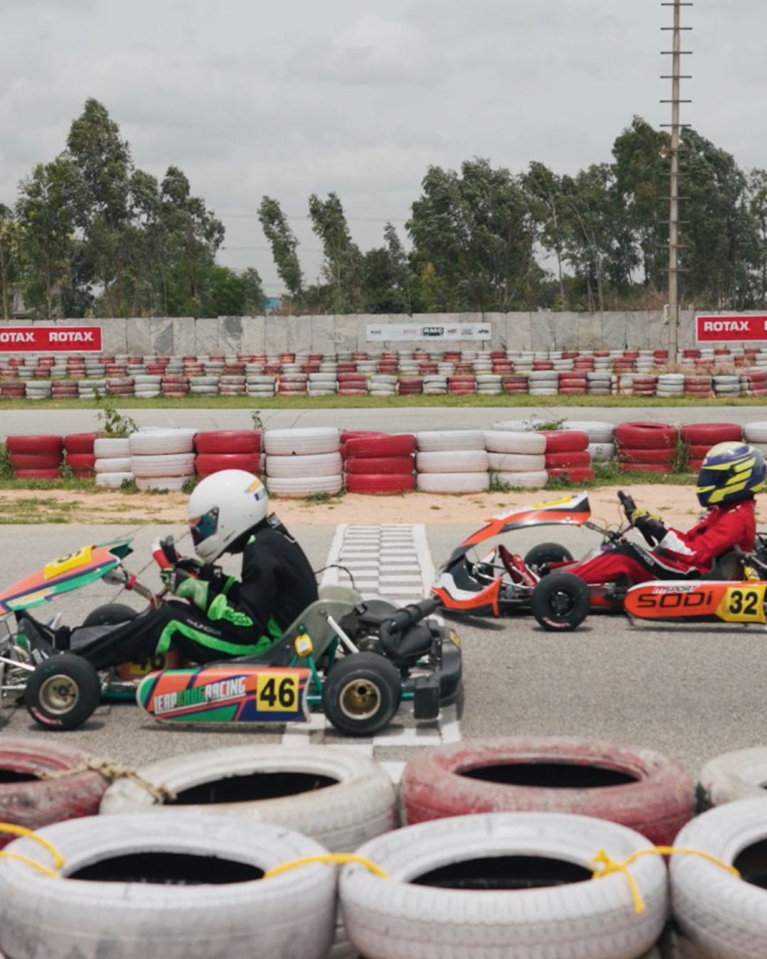 Two go-karts racing side by side near tire barriers.